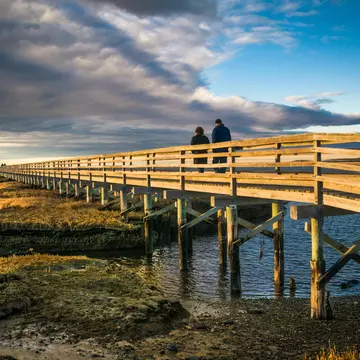 A couple walk along a boardwalk on a winter's day with the sun low in the sky