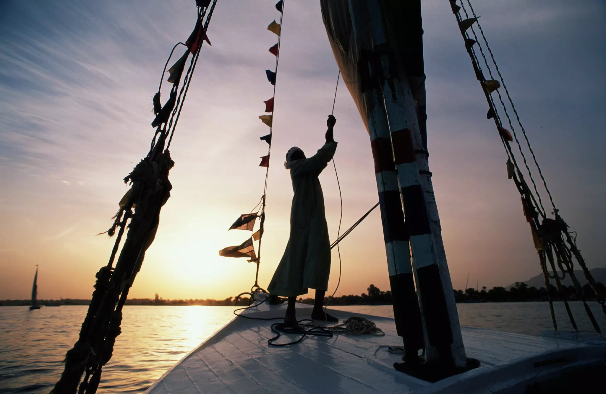 A man sailing a felucca on a river at sunset