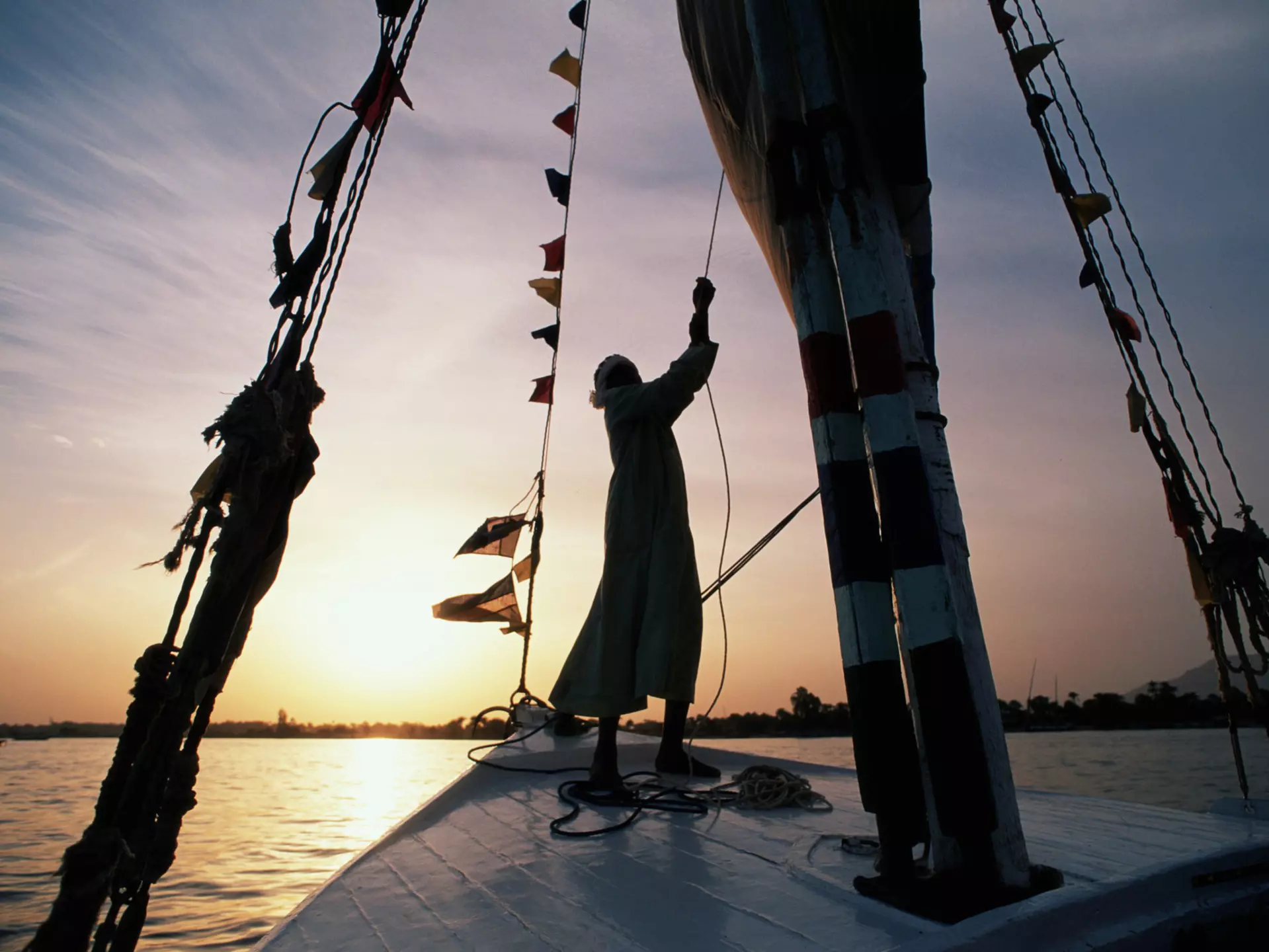 A man sailing a felucca on a river at sunset
