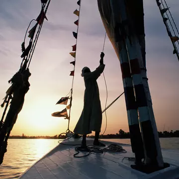 A man sailing a felucca on a river at sunset