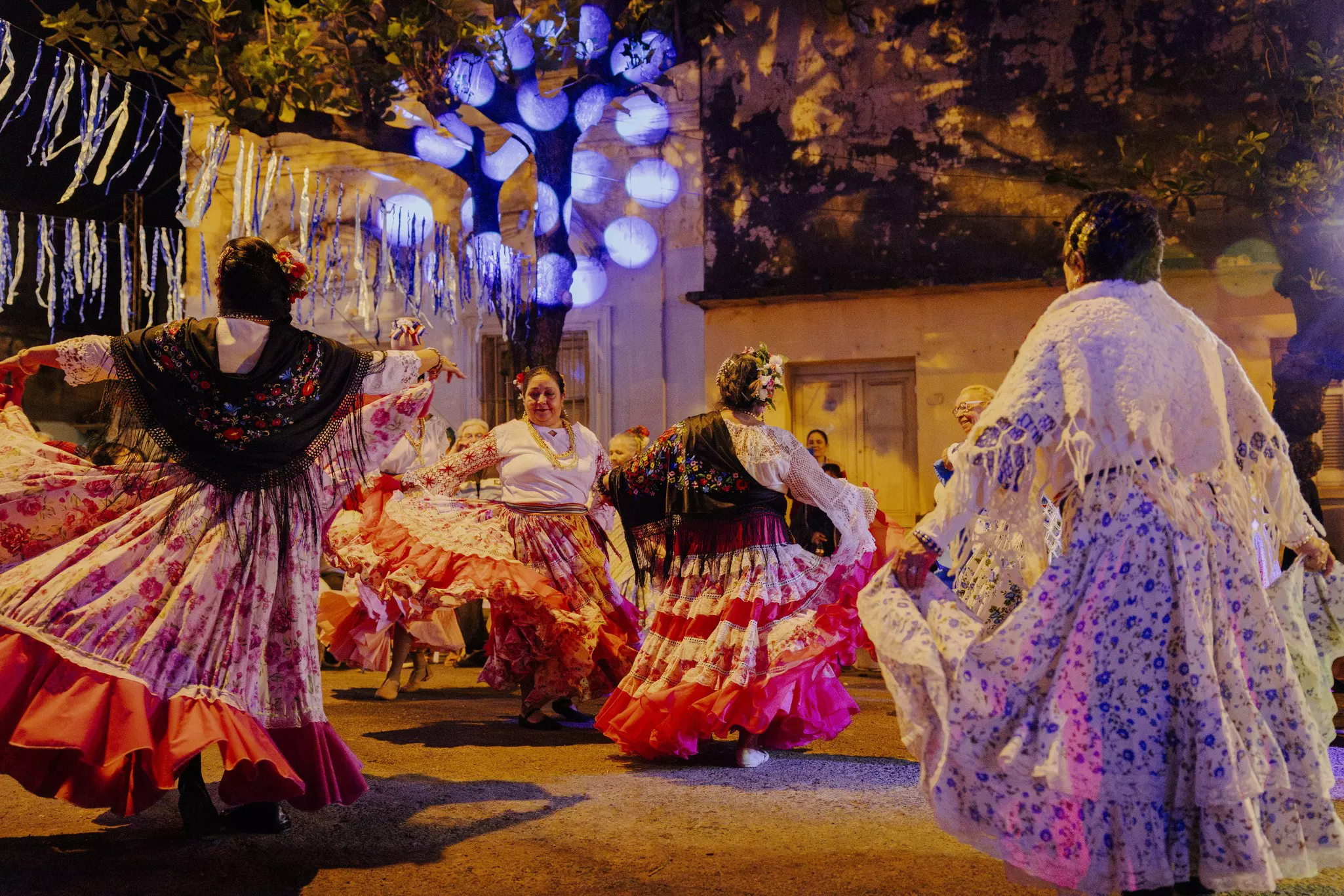 Female dancers in ruffled skirts and shawls perform on a city street after dark.