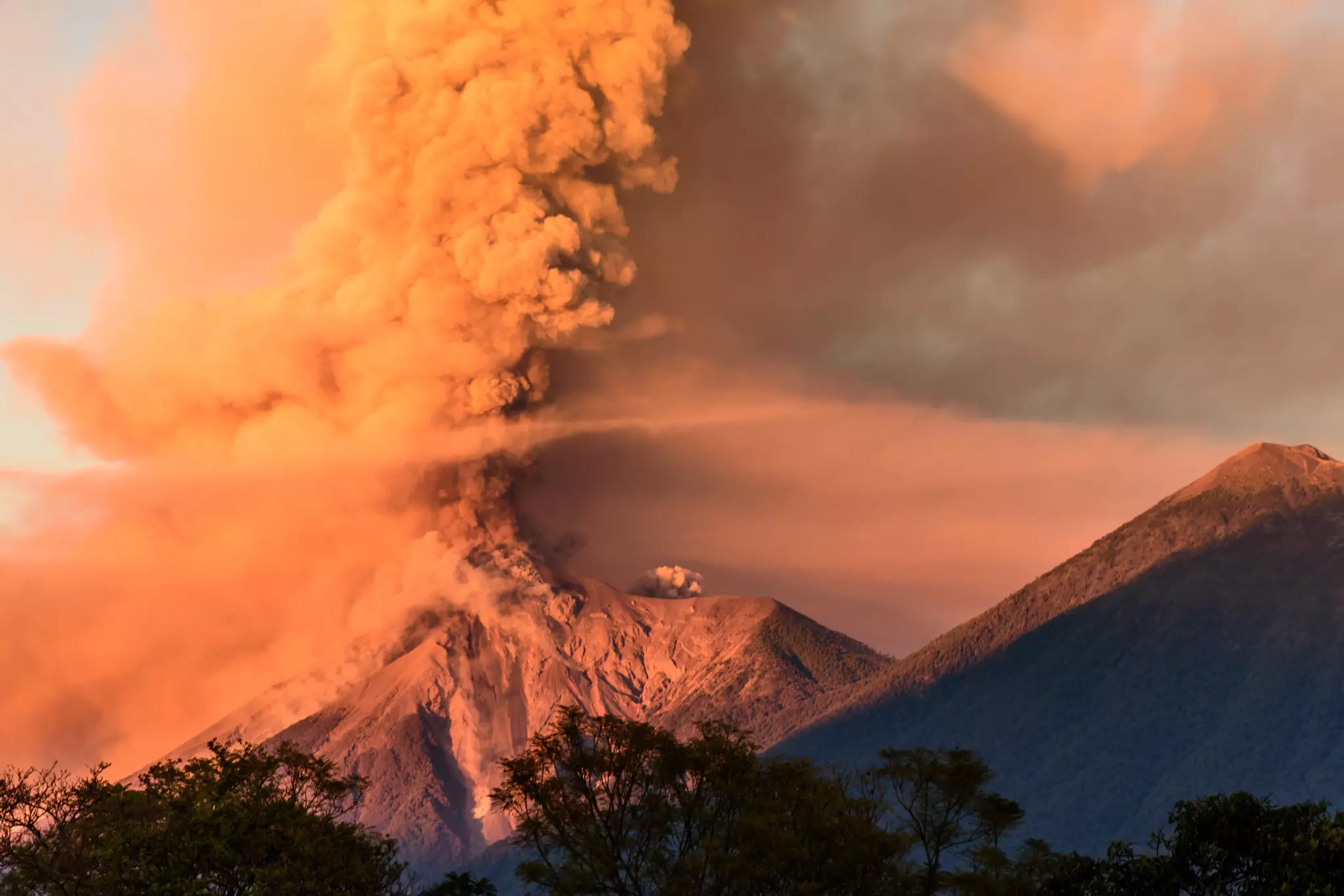 A volcano erupting at dawn next to a dormant volcano.