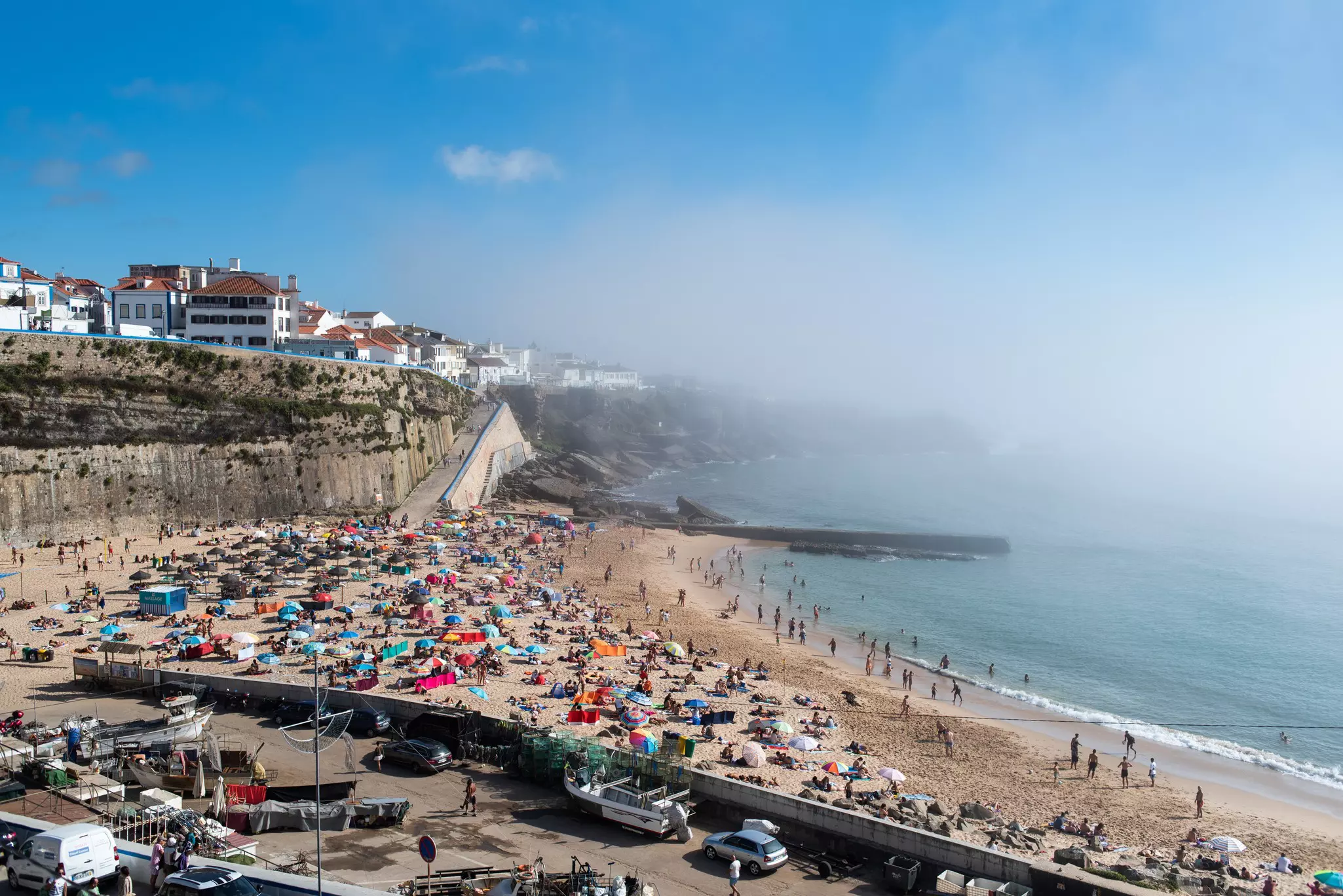 A busy beach on a summer's day with mist rolling in from the ocean.