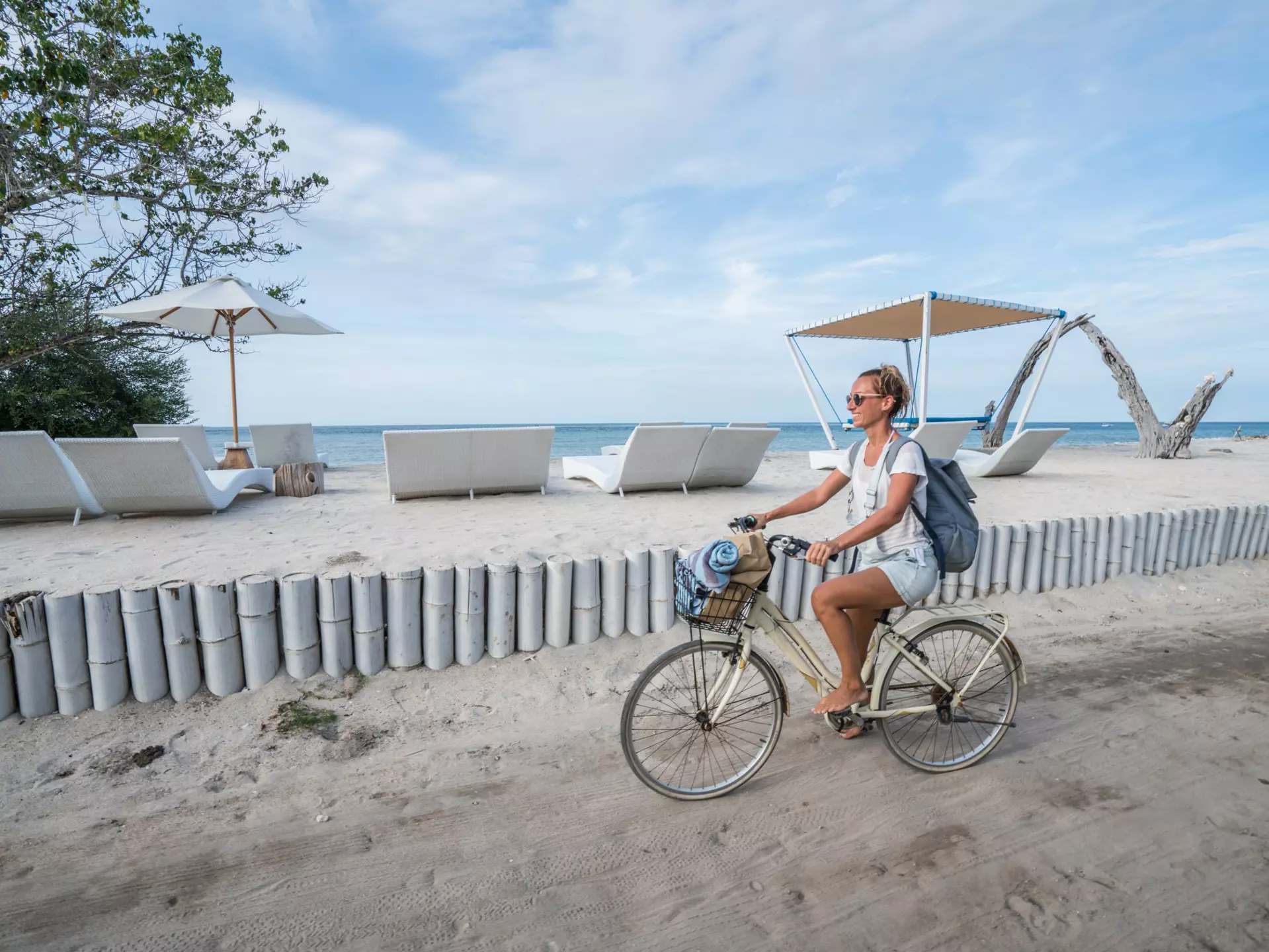 Smiling woman cycling on the beach during the morning in the Gili Islands.