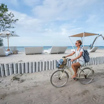 Smiling woman cycling on the beach during the morning in the Gili Islands.