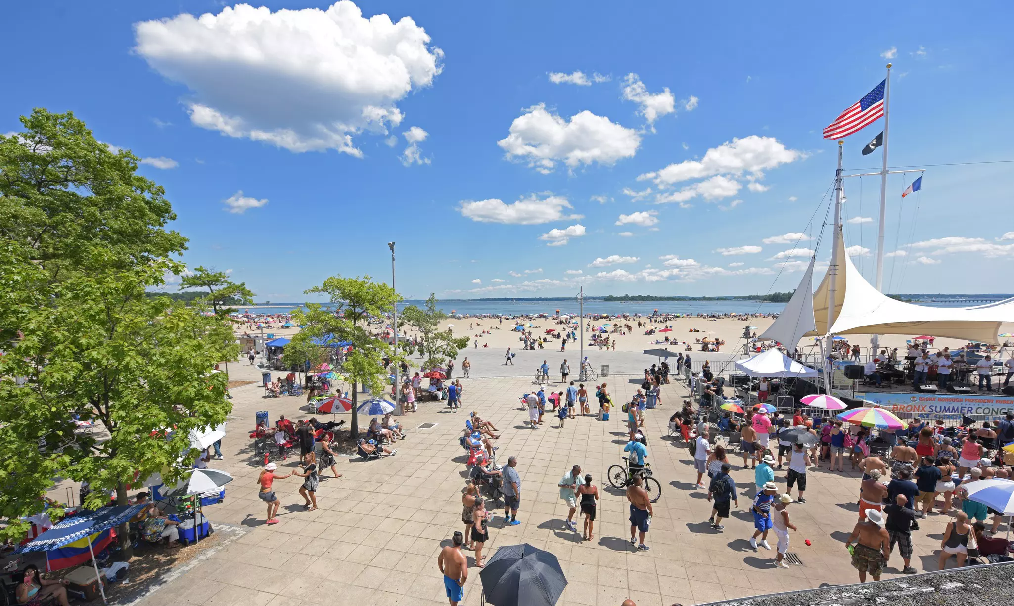 People by a sandy beach near a large white tent.
