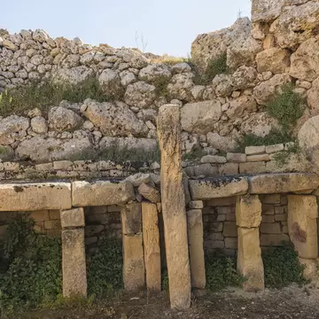 Rows of upright limestone slabs supporting long lintels, backed by a massive drystone wall of rough boulders.