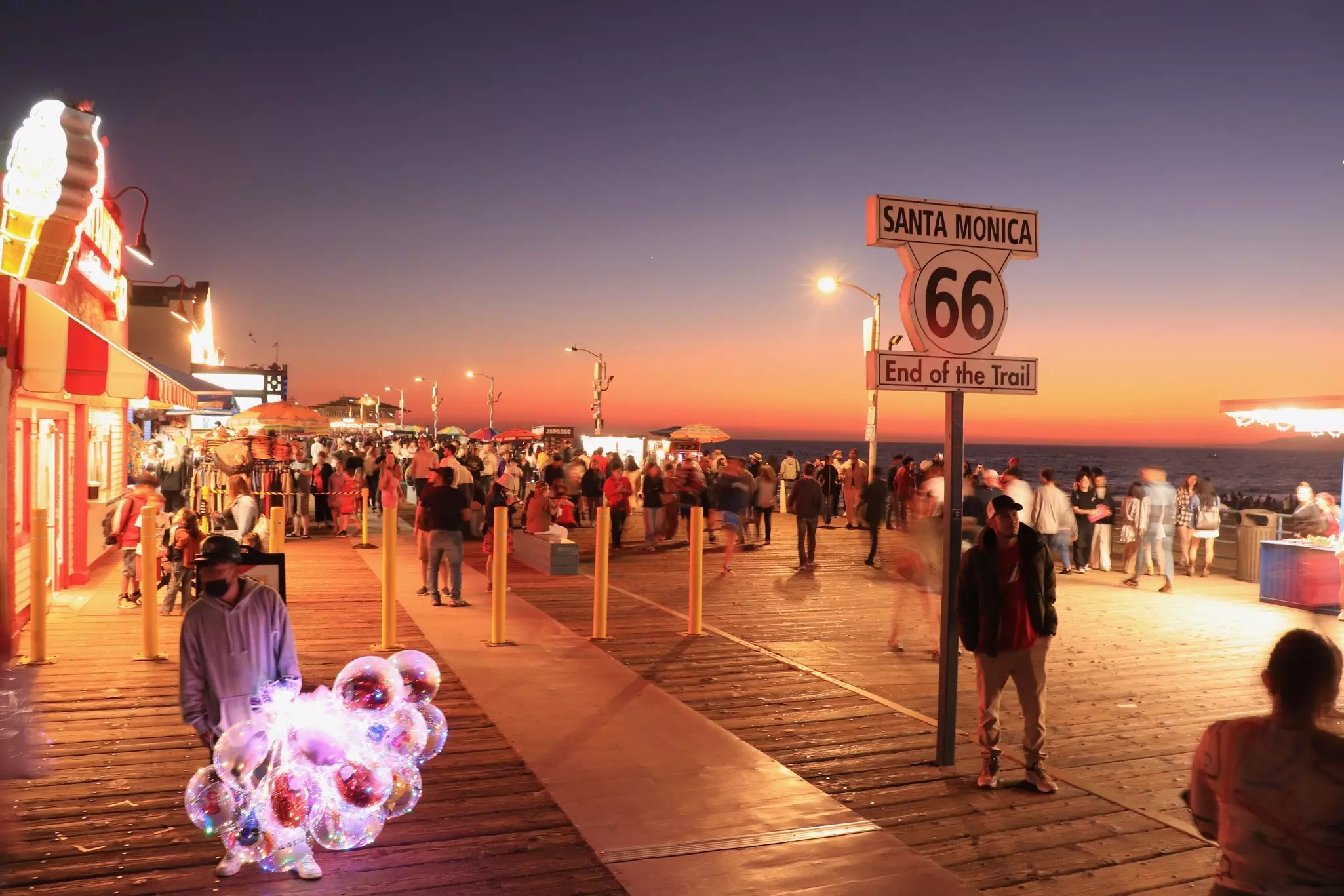 People wander on a pier with amusements and games at sunset.