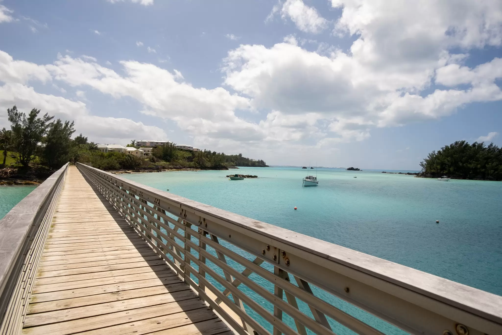 A walkway with a railing by a turquoise body of water.