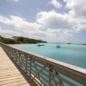 A walkway with a railing by a turquoise body of water.