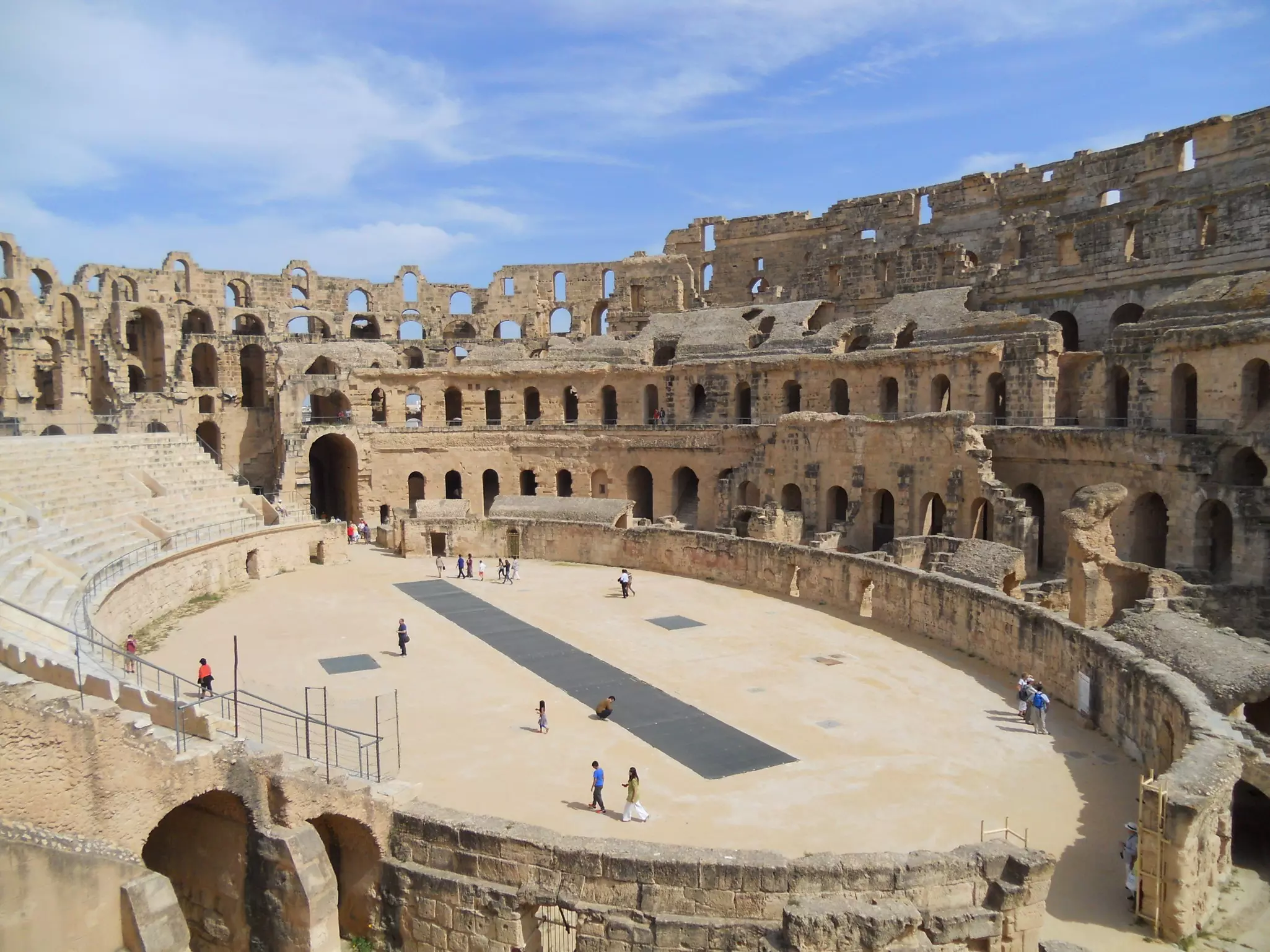 Ruins of a large amphitheater with people walking around the arena