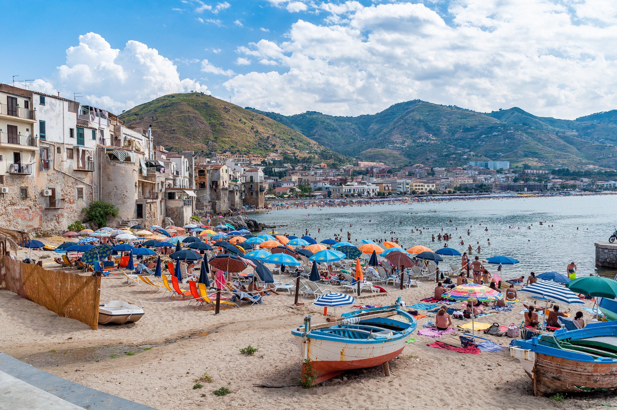 Colorful umbrellas and boats on a beach by a coastal town.