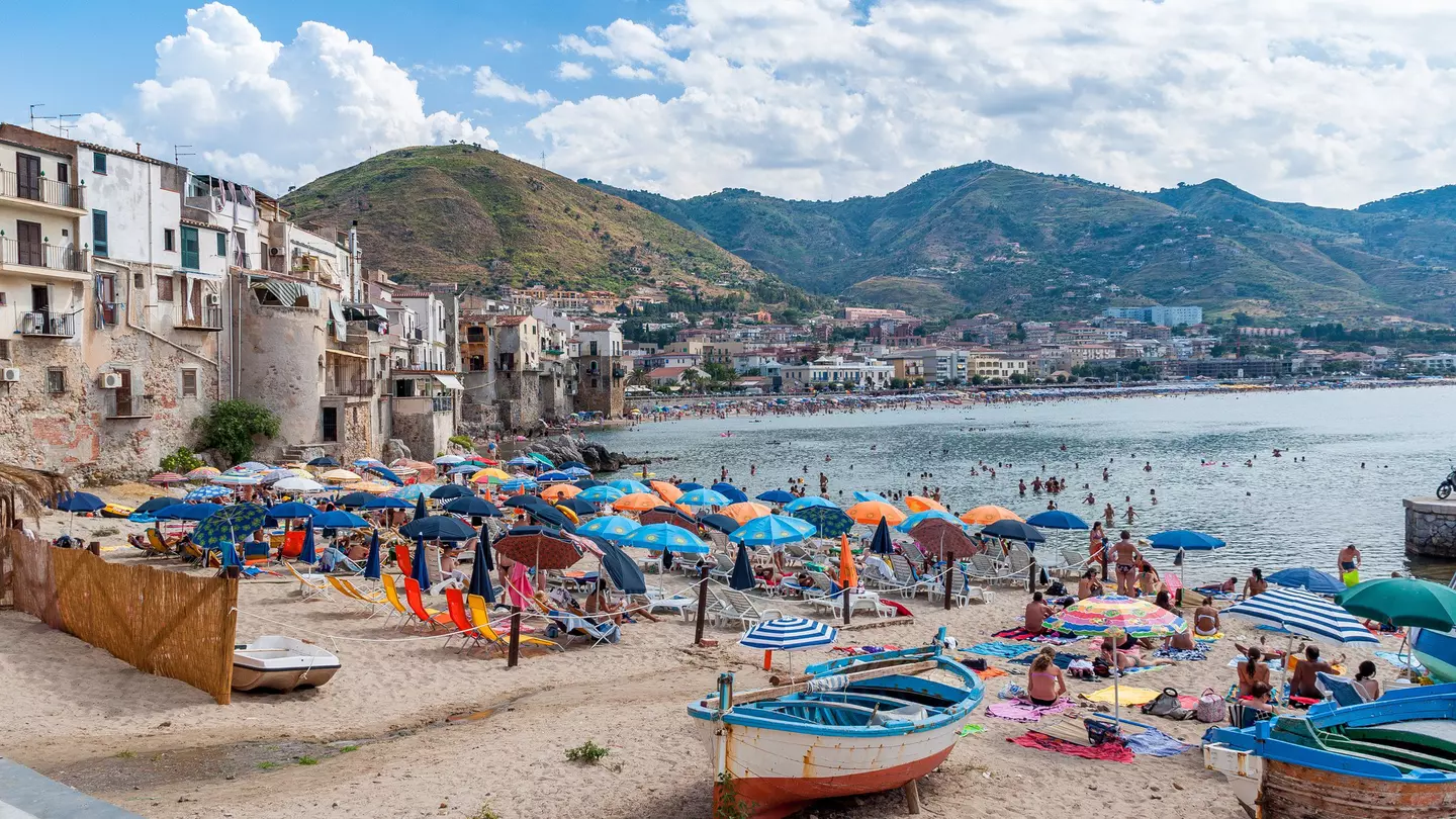 Colorful umbrellas and boats on a beach by a coastal town.