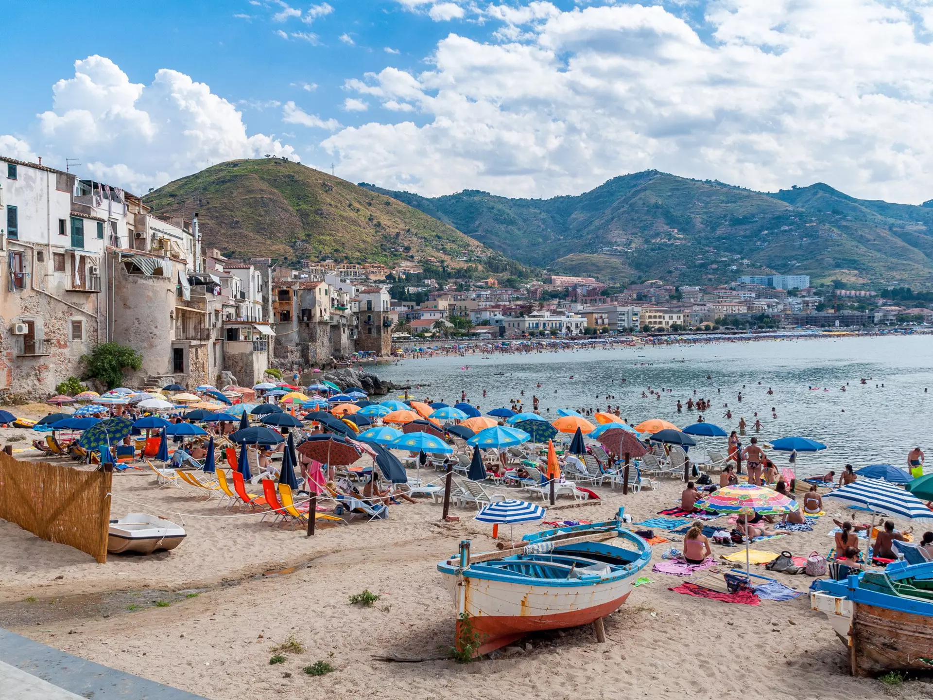 Colorful umbrellas and boats on a beach by a coastal town.