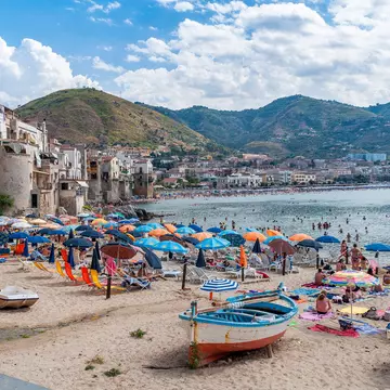 Colorful umbrellas and boats on a beach by a coastal town.