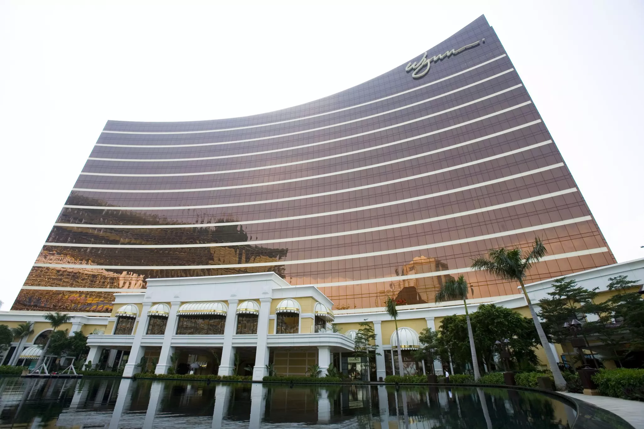 A Wynn Resorts building featuring casinos inside, with trees and a pond in the foreground.