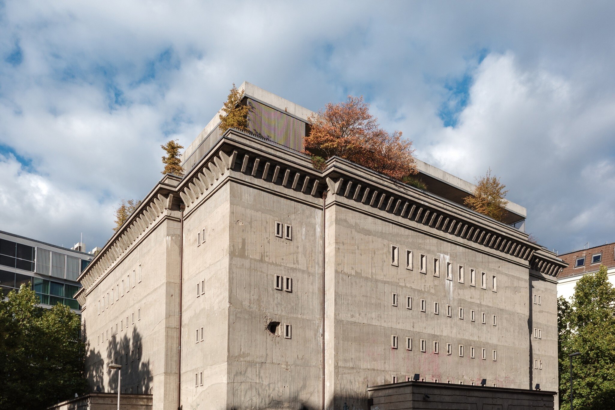 A low-angle exterior shot of the Boros Collection, a repurposed concrete World War II bunker in Berlin, Germany, featuring a rooftop garden and stark architectural lines under a bright, partly cloudy sky.
