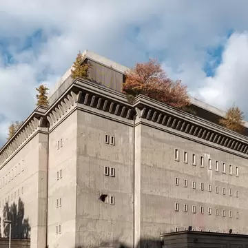 A low-angle exterior shot of the Boros Collection, a repurposed concrete World War II bunker in Berlin, Germany, featuring a rooftop garden and stark architectural lines under a bright, partly cloudy sky.