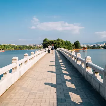 Couple walking a white stone bridge across the lake in Fukuoka's Ohori Park, with city towers beyond