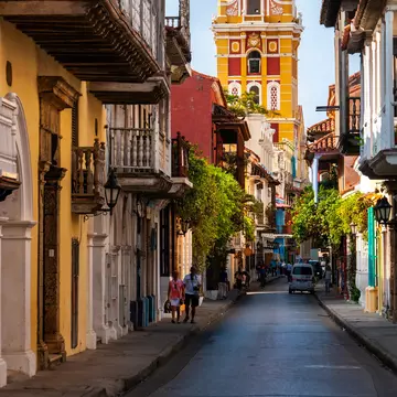 A yellow tower against blue sky at the end of a narrow street in a town's historic center.