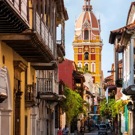 A yellow tower against blue sky at the end of a narrow street in a town's historic center.