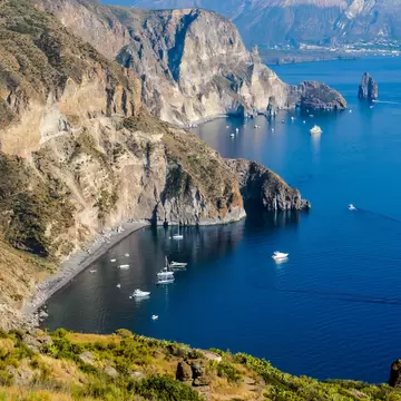Aerial iew of Valle Muria beach in Lipari and the Faraglioni. In the background the crater of Vulcano Island. Aeolian islands, Sicily