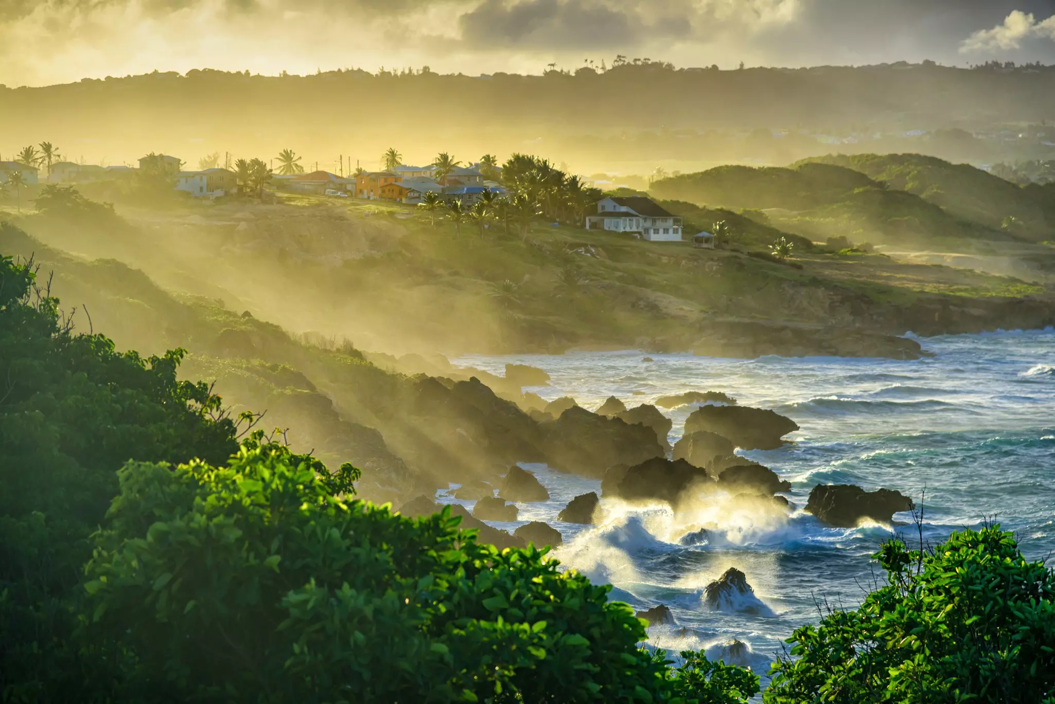 Water sprays up as waves crash on land at a rocky beach at sunset.