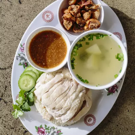 A plate of white meat chicken with a cup of soup and two sauces in bowls all together on an oval plate.