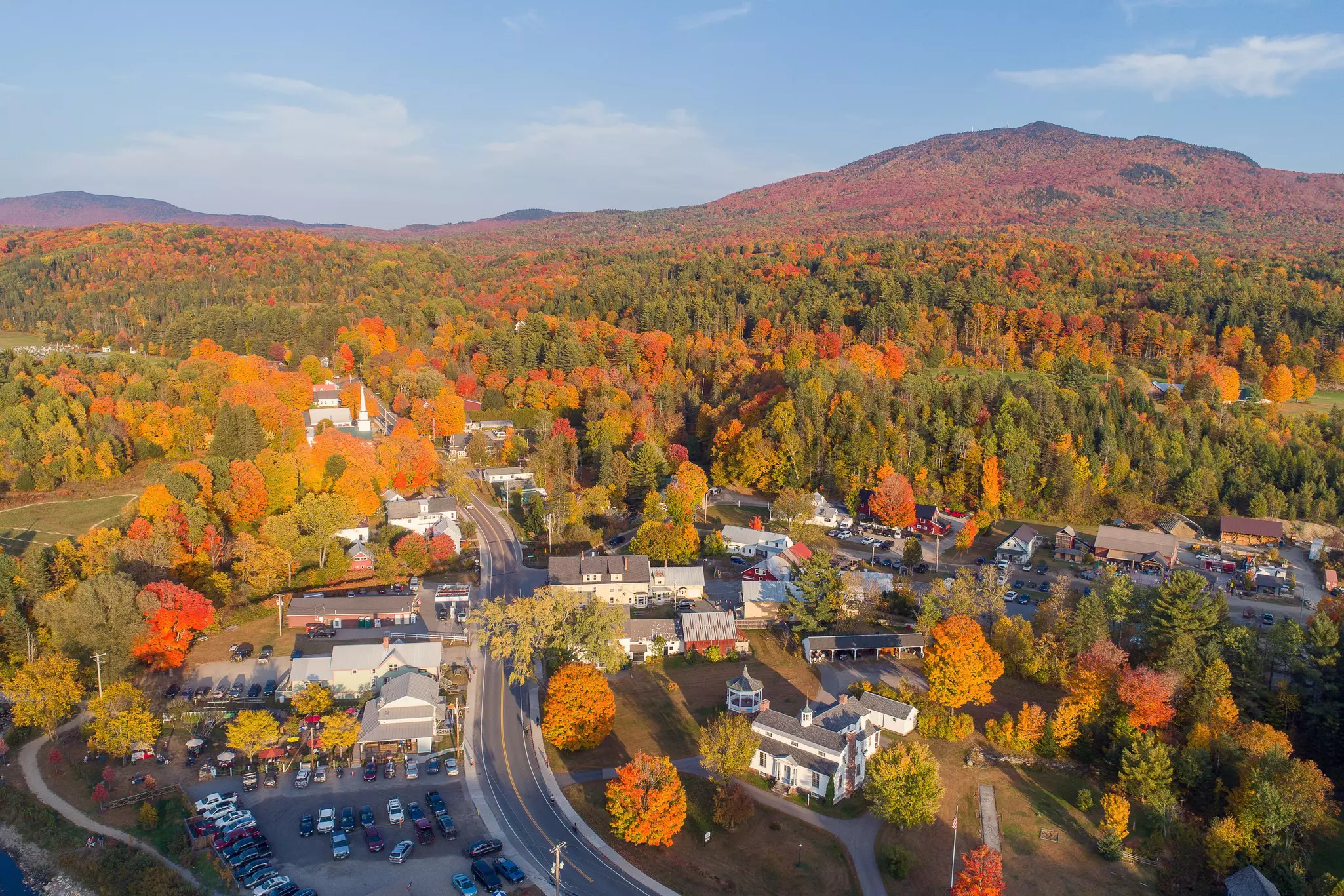 A road through a village into woodland with leaves on trees changing from dark green to yellow, red, orange and gold.