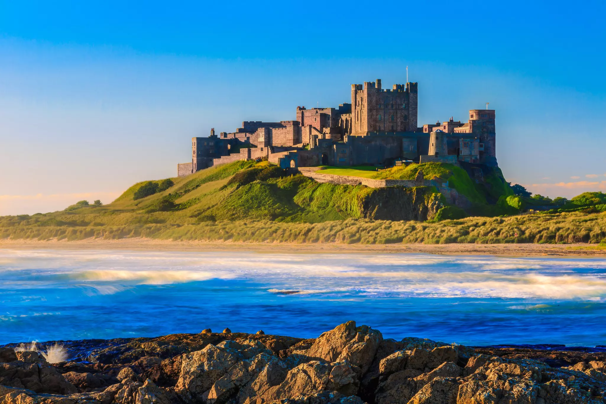 Bamburgh Castle, with blue water and sunlit rocks