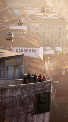 People at the edge of a railing at sunset, high above the buildings below; three cars on the cable of gondola are in the background. 