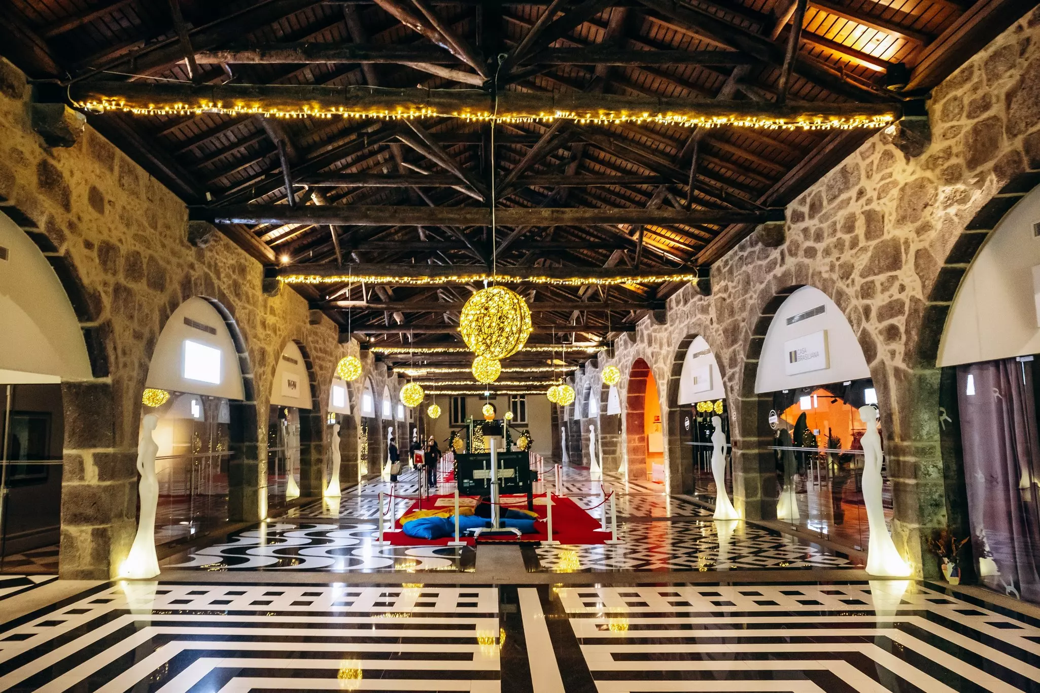 A hall of storefronts lined with mannequins and string lights