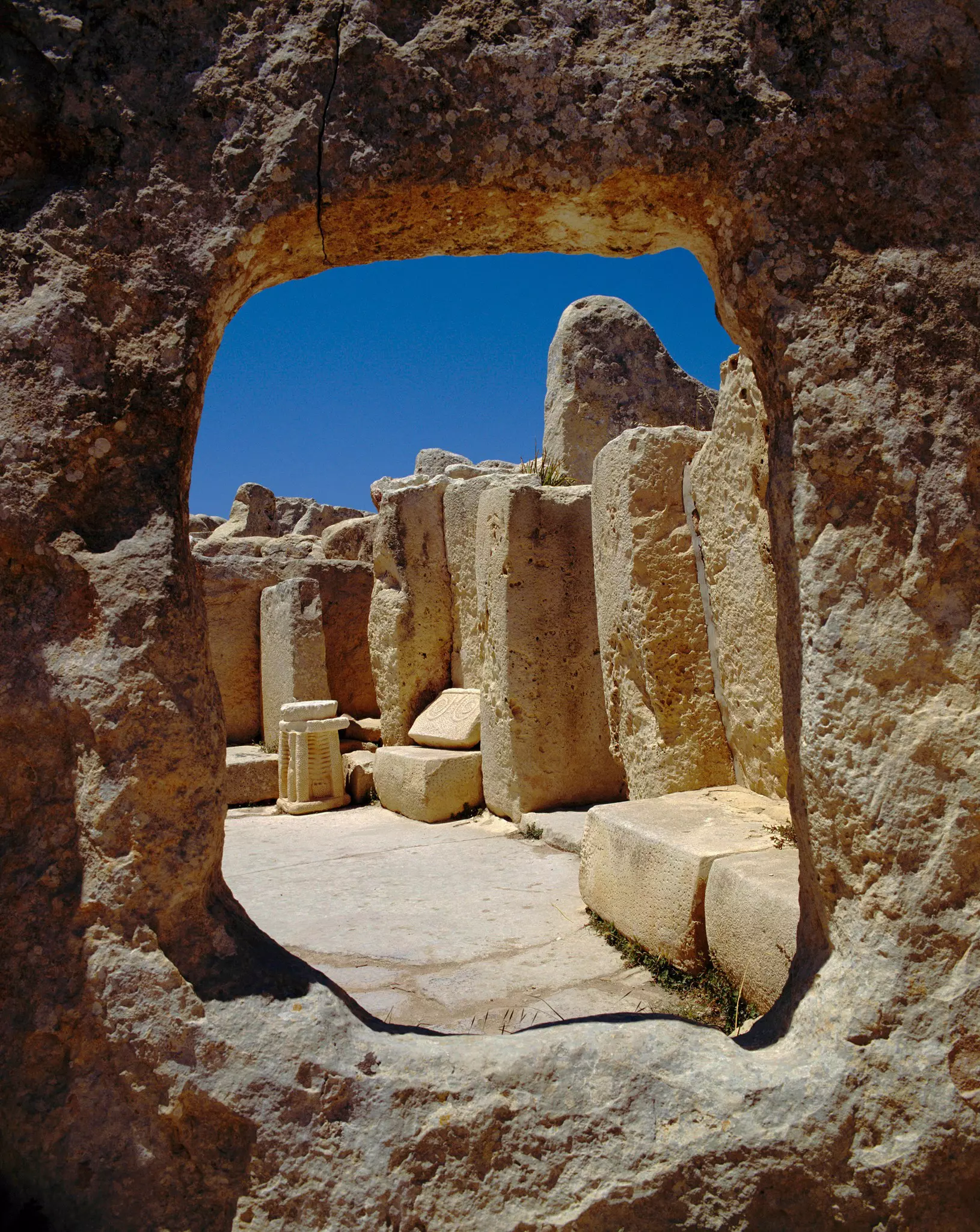 A large round window through stone towards a collection of ancient stones and engravings in the ruins of a prehistoric temple.