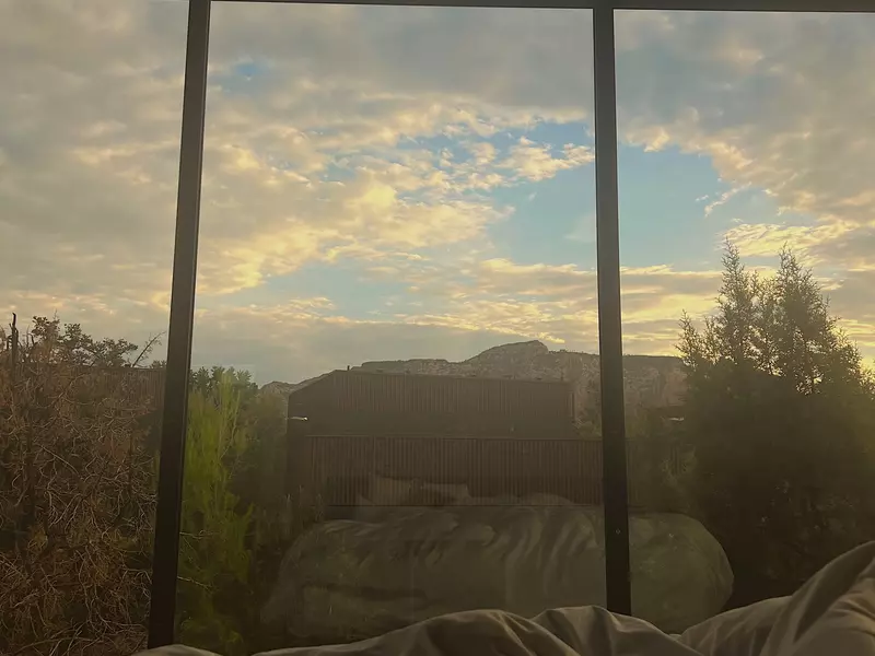 Silhouettes of rock formations in morning light through a window from a hotel bed.