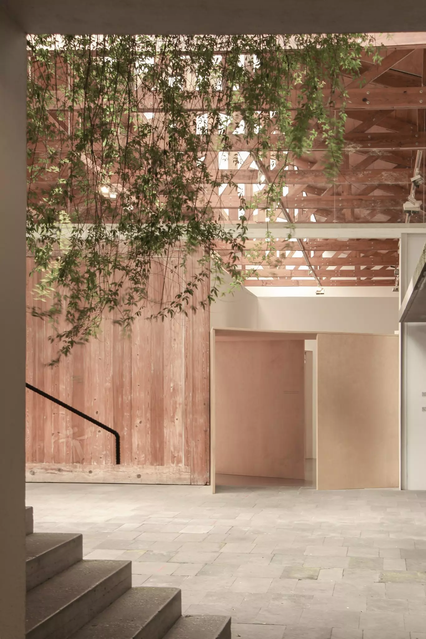 The stylish entrance to an art gallery, with modern wooden paneling and plants growing through the latticed roof