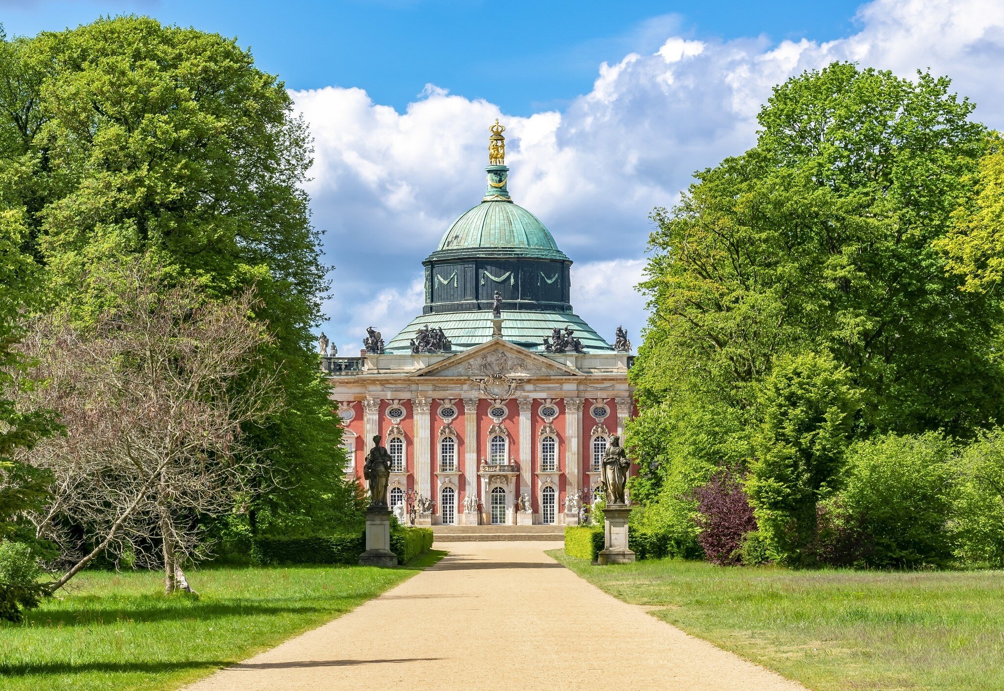 Exterior of New Palace (Neues Palais) framed by trees and two statues in Sanssouci park, Potsdam, Germany.