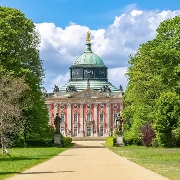 Exterior of New Palace (Neues Palais) framed by trees and two statues in Sanssouci park, Potsdam, Germany.