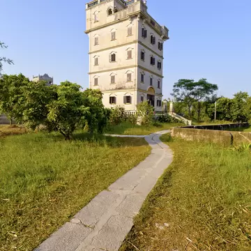 Tall pale fortified tower house with shuttered windows and a balustraded top, a stone path leading to it, Kaiping.