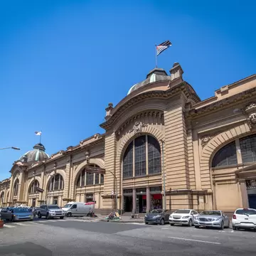Sandstone market hall with arched stained-glass windows, a flag-topped dome and cars parked along the street