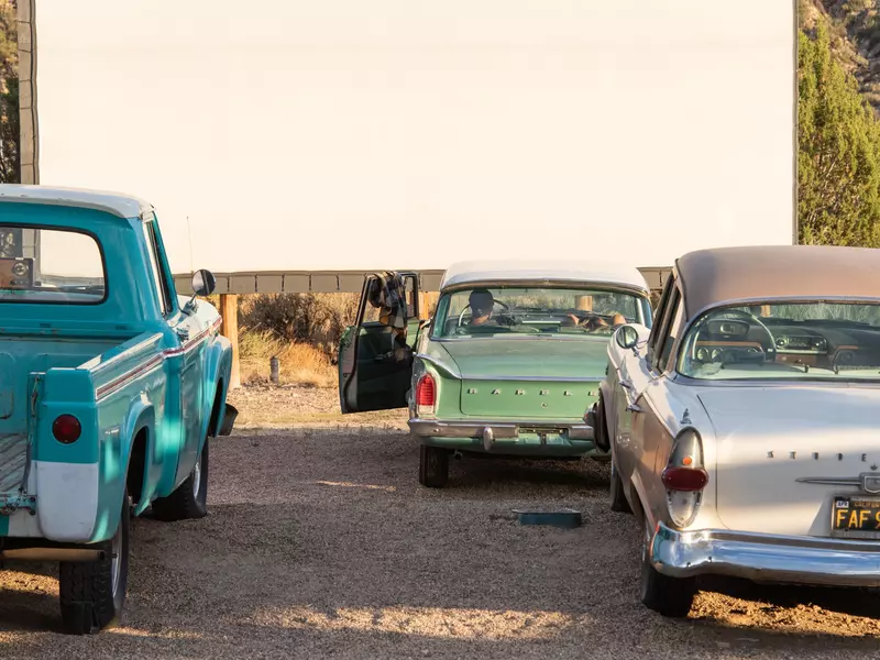 Three old cars from the 1950's are parked in front of a giant screen