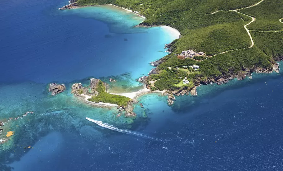 Aerial view of a lush green headland, coral-fringed coves and a speeding boat cutting through deep blue sea