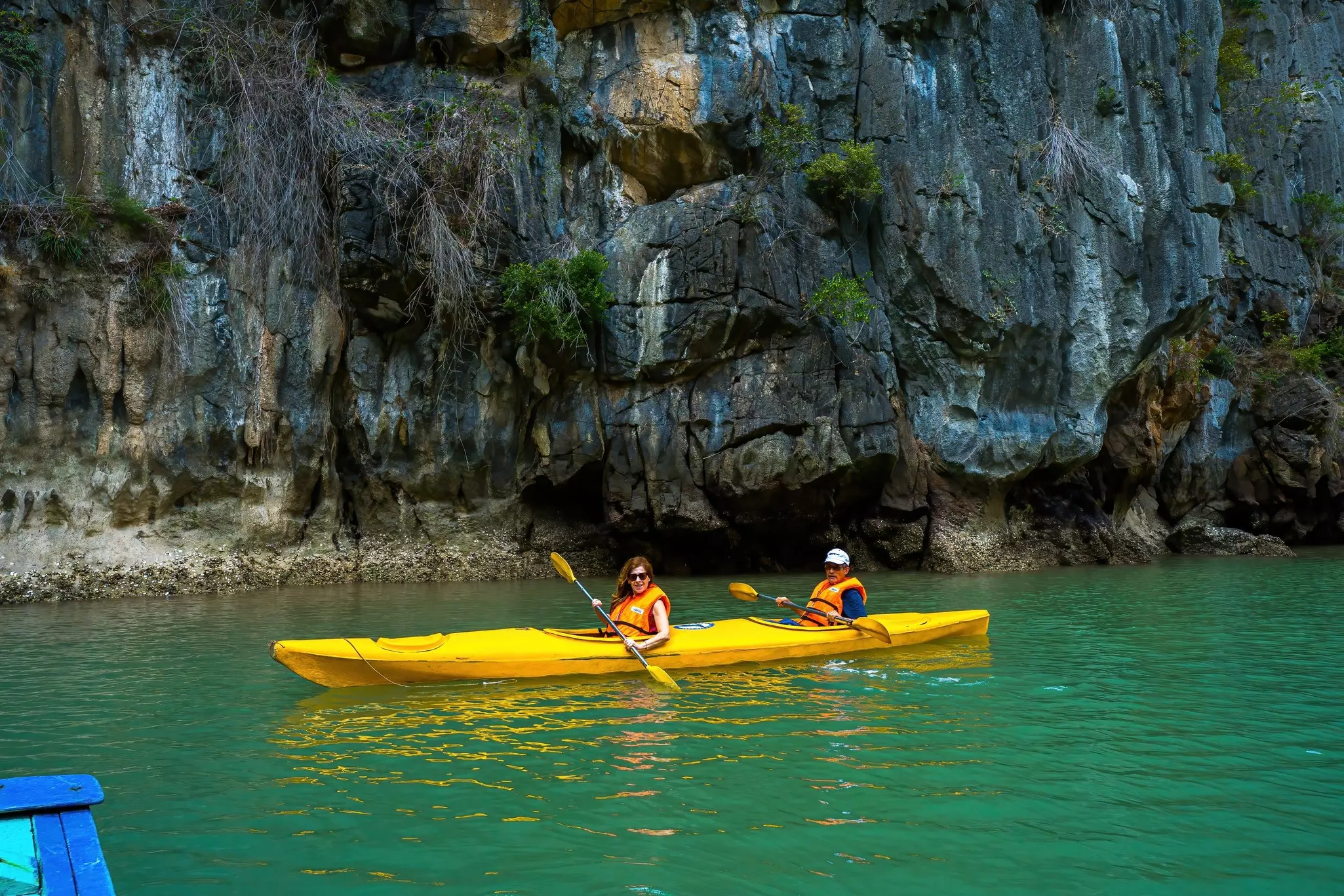 Two people in a yellow kayak among limestone rocks at Halong Bay
