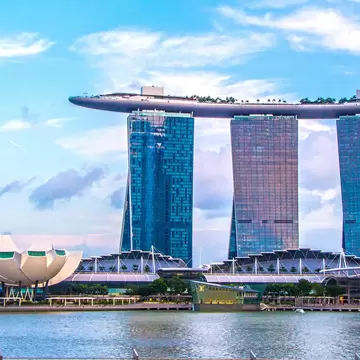 Three tall hotel towers joined by a ship-shaped rooftop deck, beside a white lotus-shaped museum across calm water.