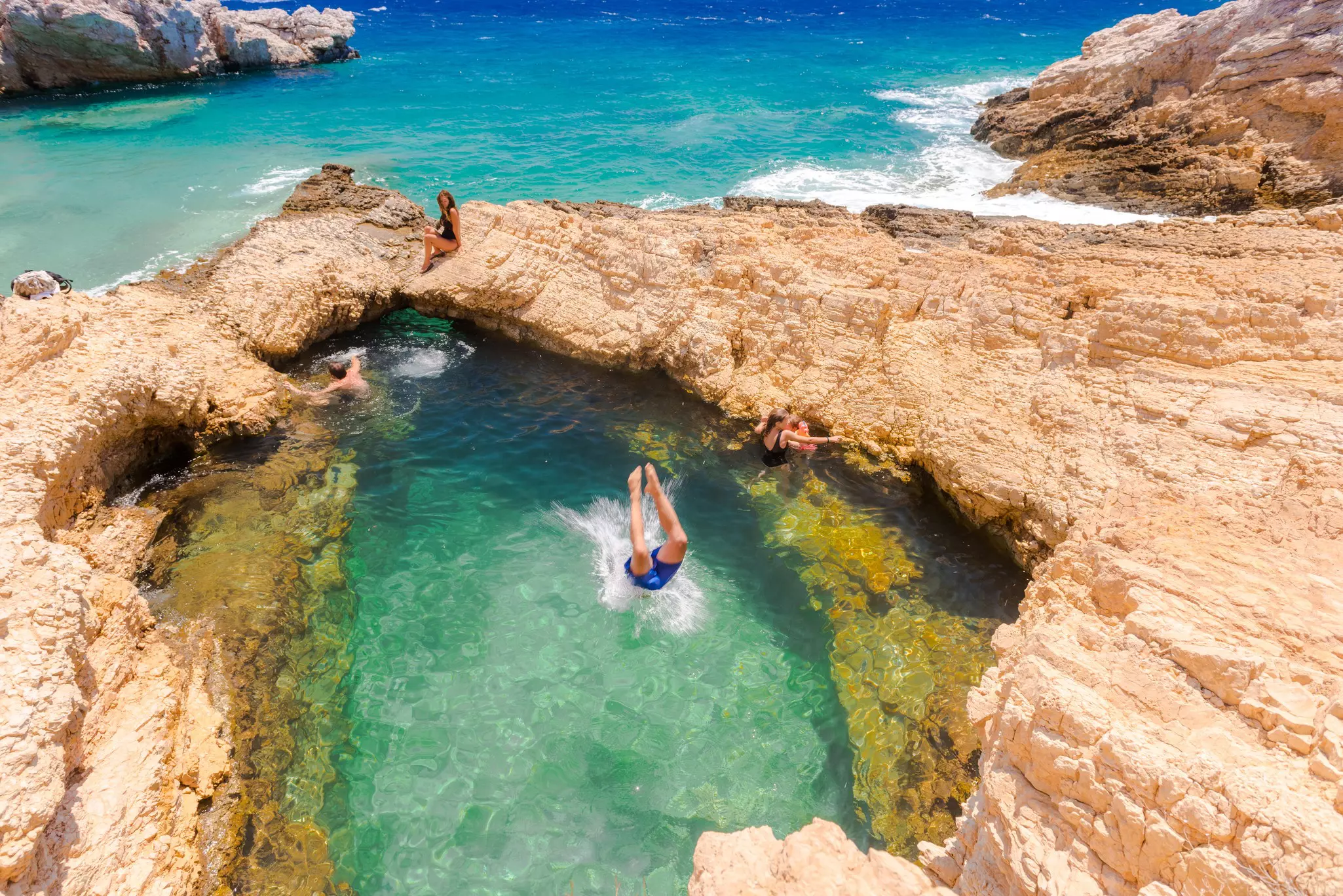 People in a natural pool of clear water in rocks on a shore