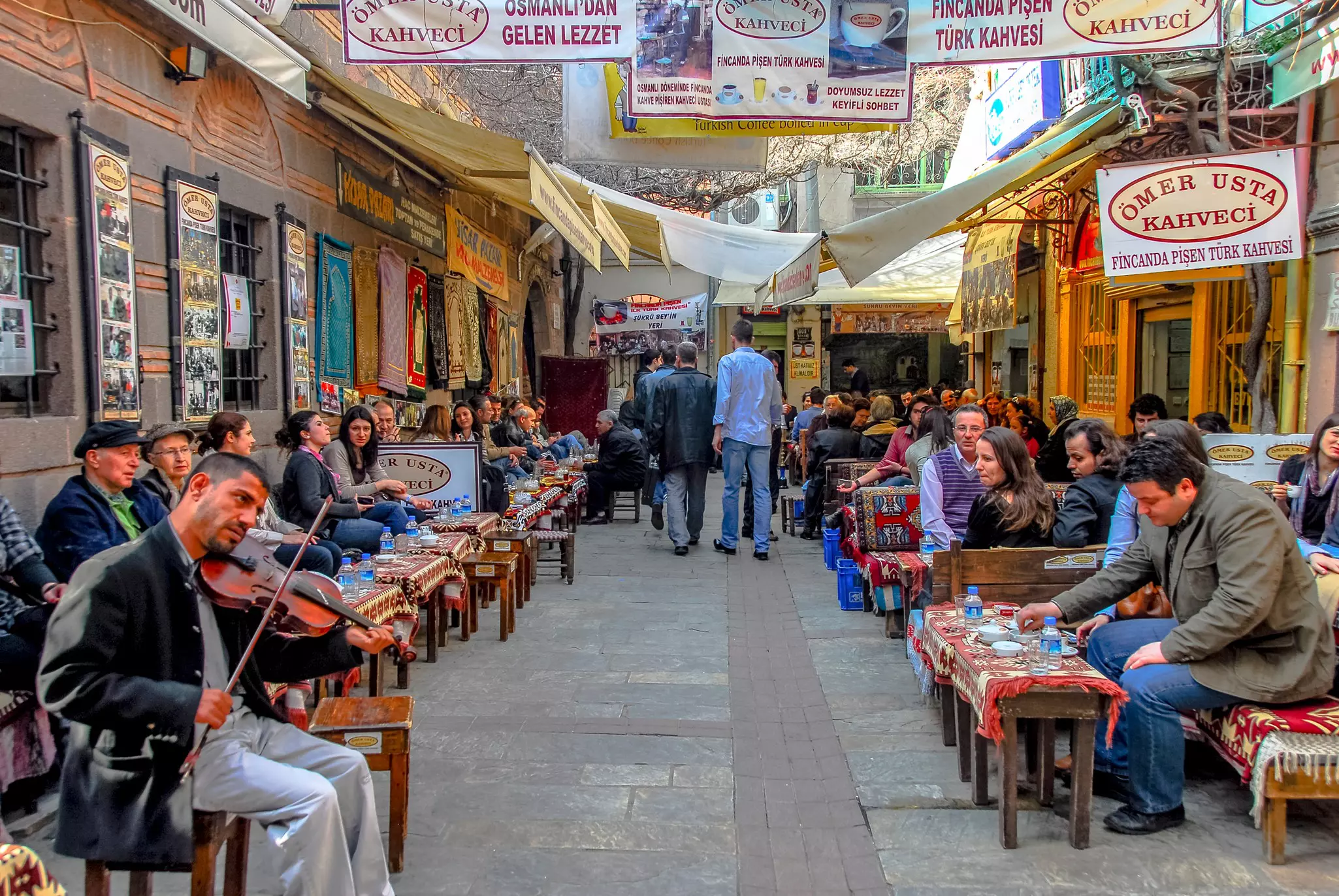 People sit on cushioned benches outside that line a wide passageway outside a coffeeshop