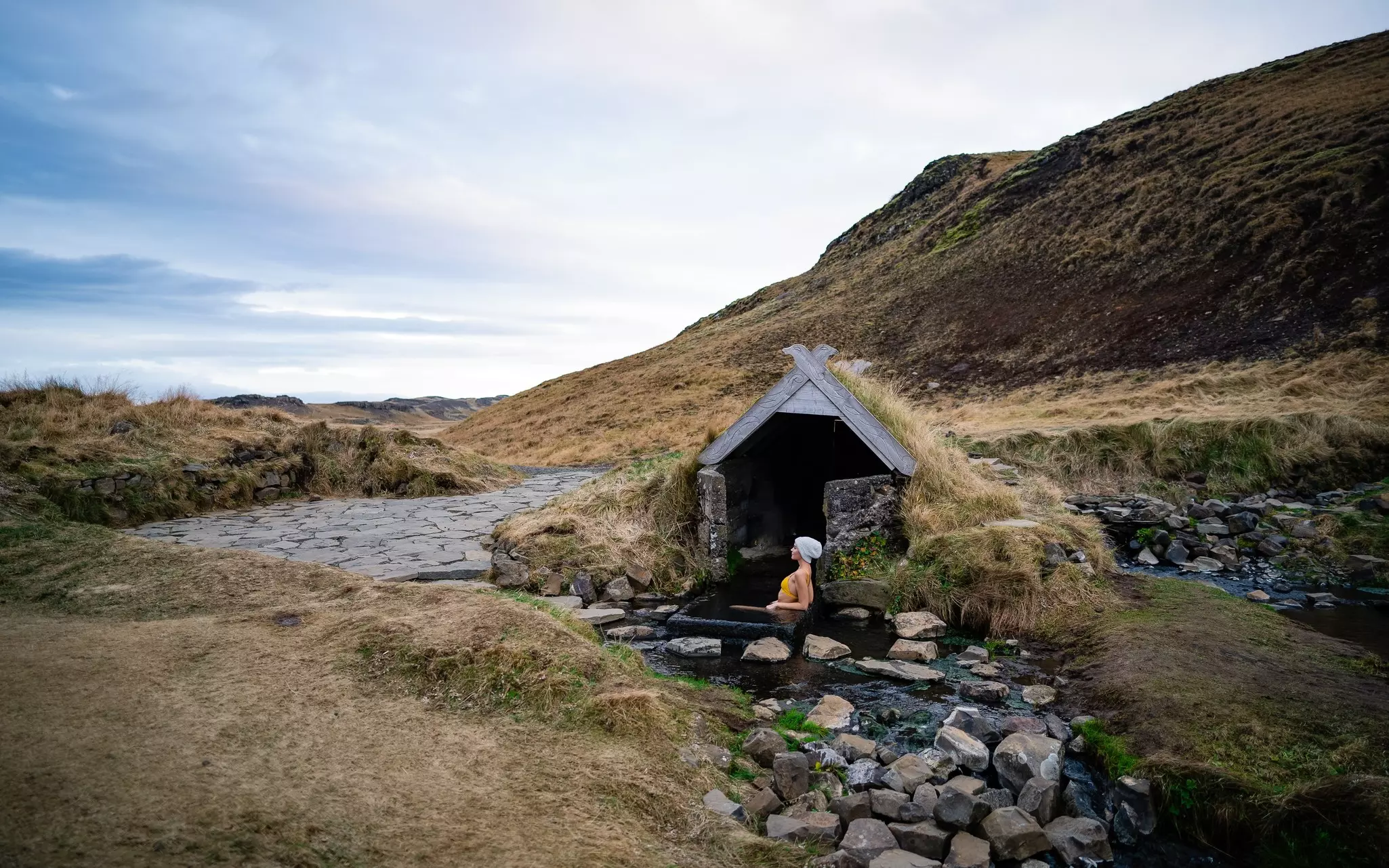 A woman soaks in an outdoor hot spring in the shelter of a tiny stone house