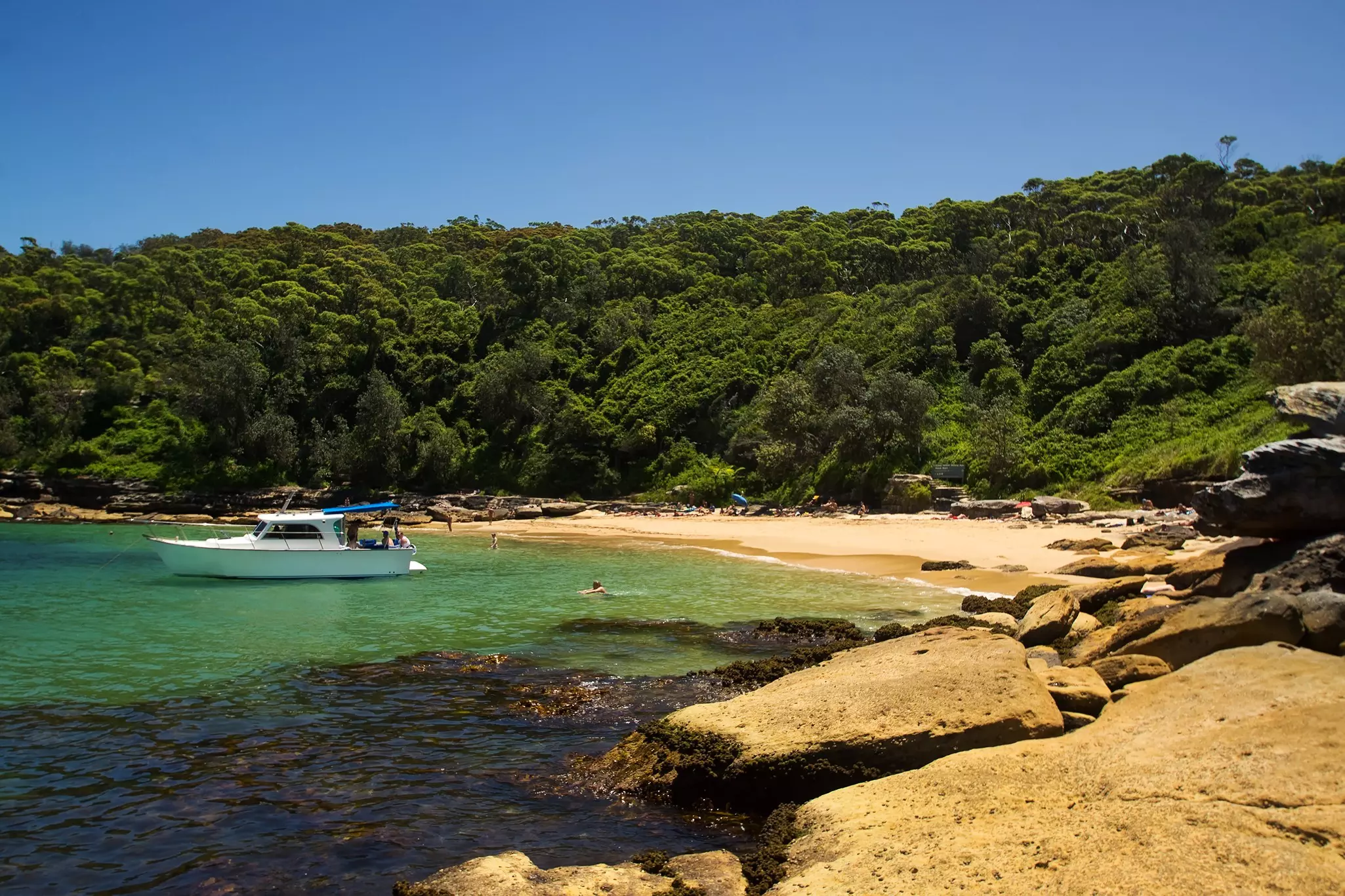 A sheltered cove of golden sand. A boat is moored in the shallows.