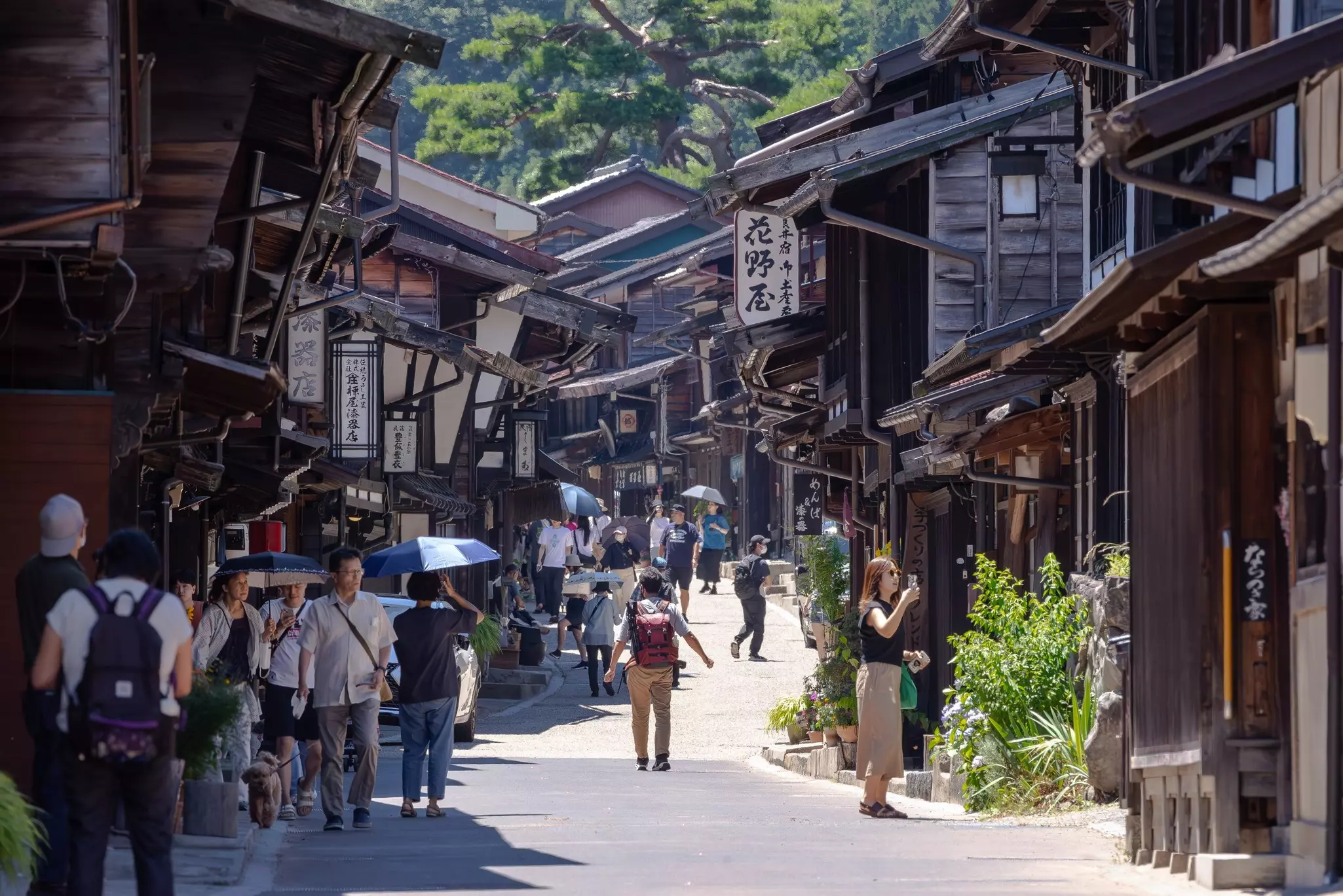 Tight road lined with wooden Japanese structures and lined with walkers