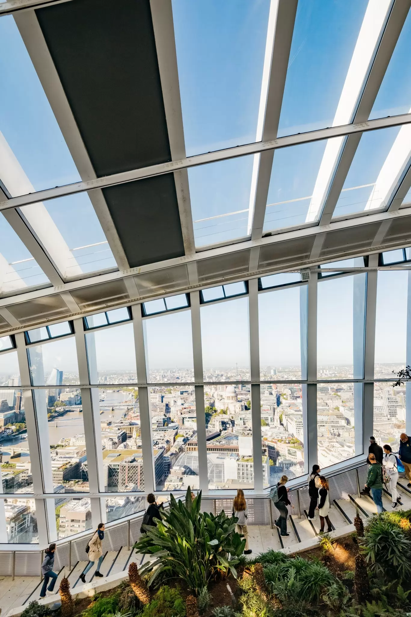 Visitors walk up stairs within a vast conservatory on a high floor with views of the city below: Sky Garden, London