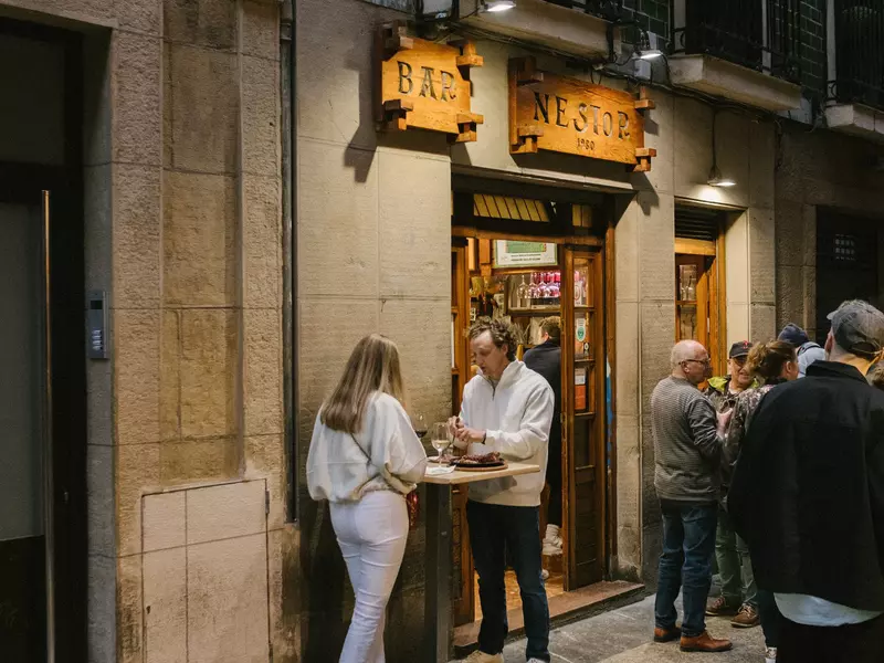 Customers dine standing at tables outside a restaurant
